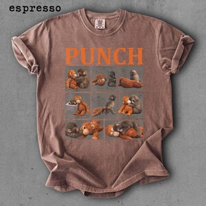 Peut inclure: T-shirt couleur expresso avec le mot "PUNCH" en lettres orange. Le t-shirt pr&eacute;sente une grille de neuf carr&eacute;s, chacun contenant une illustration diff&eacute;rente de singes. Le t-shirt est fait d'une mati&egrave;re douce et confortable.