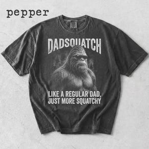 May include: Dark gray t-shirt with the text "DADSQUATCH" above an illustration of a Bigfoot wearing sunglasses. Below the illustration, the text reads "LIKE A REGULAR DAD, JUST MORE SQUATCHY". The word "pepper" is in the upper left corner.