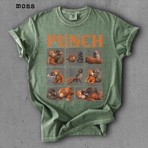 Peut inclure: T-shirt vert avec le mot "PUNCH" en lettres orange. Le t-shirt pr&eacute;sente une grille de neuf carr&eacute;s, chacun avec une illustration diff&eacute;rente de singes. Le t-shirt est de couleur vert mousse.