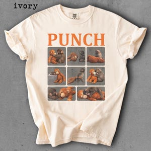 Peut inclure: T-shirt ivoire avec le mot "PUNCH" en lettres orange. En dessous, neuf carr&eacute;s avec des illustrations d'orang-outans. Le t-shirt est en mati&egrave;re douce.