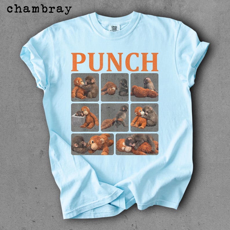 Peut inclure: T-shirt bleu clair avec le mot "PUNCH" en lettres orange. Le t-shirt pr&eacute;sente une grille de neuf carr&eacute;s, chacun avec une illustration diff&eacute;rente de singes. Le t-shirt est fait d'une mati&egrave;re douce et confortable.