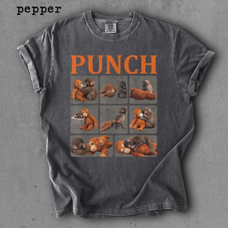 Peut inclure: T-shirt gris fonc&eacute; avec des manches retrouss&eacute;es. Le mot "PUNCH" en lettres orange est imprim&eacute; au-dessus d'une grille de singes de dessins anim&eacute;s. Les singes sont dans diverses poses, certains se c&acirc;linant et d'autres allong&eacute;s.