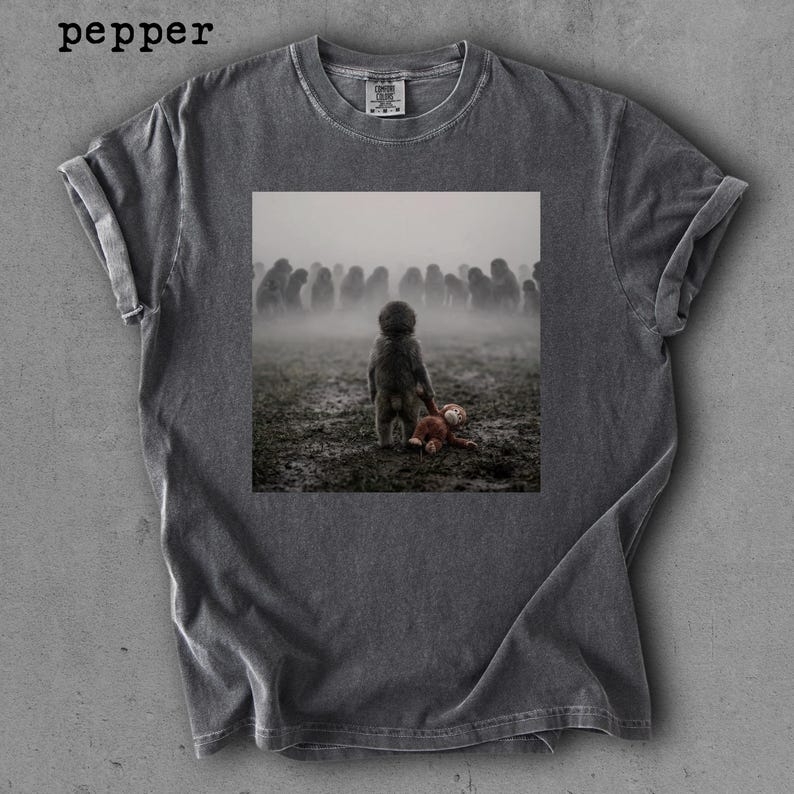 May include: Dark gray t-shirt with a printed image of a child holding a teddy bear in a field with a crowd of people in the background. The word "pepper" is printed in the upper left corner.
