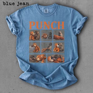 Peut inclure: T-shirt bleu jean avec le mot "PUNCH" en lettres orange. Le t-shirt pr&eacute;sente une grille de neuf carr&eacute;s, chacun avec une illustration diff&eacute;rente de singes. Le t-shirt est fait d'une mati&egrave;re douce.
