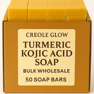 May include: A box of turmeric and kojic acid soap bars. The box is brown with a cream-colored label that reads "Creole Glow Turmeric Kojic Acid Soap Bulk Wholesale 50 Soap Bars." The soap bars are yellow and rectangular.