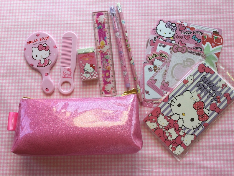 May include: Pink Hello Kitty themed pencil case with a zipper closure. The case is filled with Hello Kitty stationery including a ruler, pencils, a comb, an eraser, and stickers.