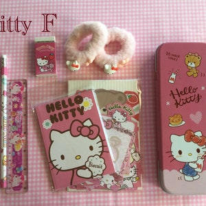 May include: A pink Hello Kitty pencil case, a pink Hello Kitty notebook, a pink Hello Kitty eraser, two pink fuzzy hair ties, a pink pencil, a pink pen, and a pink ruler with Hello Kitty and unicorn designs. The background is a pink and white gingham pattern.