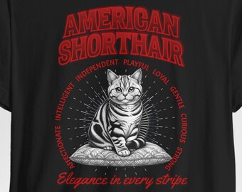 May include: Black t-shirt featuring a detailed illustration of an American Shorthair cat. The design includes the text "AMERICAN SHORTHAIR" in red, with additional descriptive words around the cat image. The phrase "Elegance in every stripe" is also present.