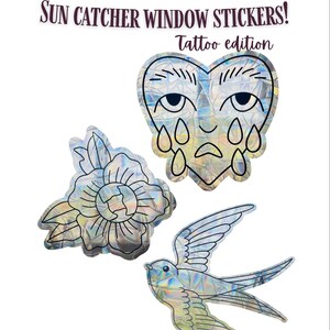 May include: Three holographic sun catcher window stickers with a tattoo theme. The text reads SUN CATCHER WINDOW STICKERS! Tattoo edition and CHLOE_MAKESX. Designs include a crying heart with eyes, a flower, and a flying swallow bird.