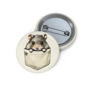 May include: A round button featuring a cute hamster peeking out of a pocket. The hamster is gray and white with big black eyes. The pocket is beige with a green tag. A second button with a silver pin is visible.