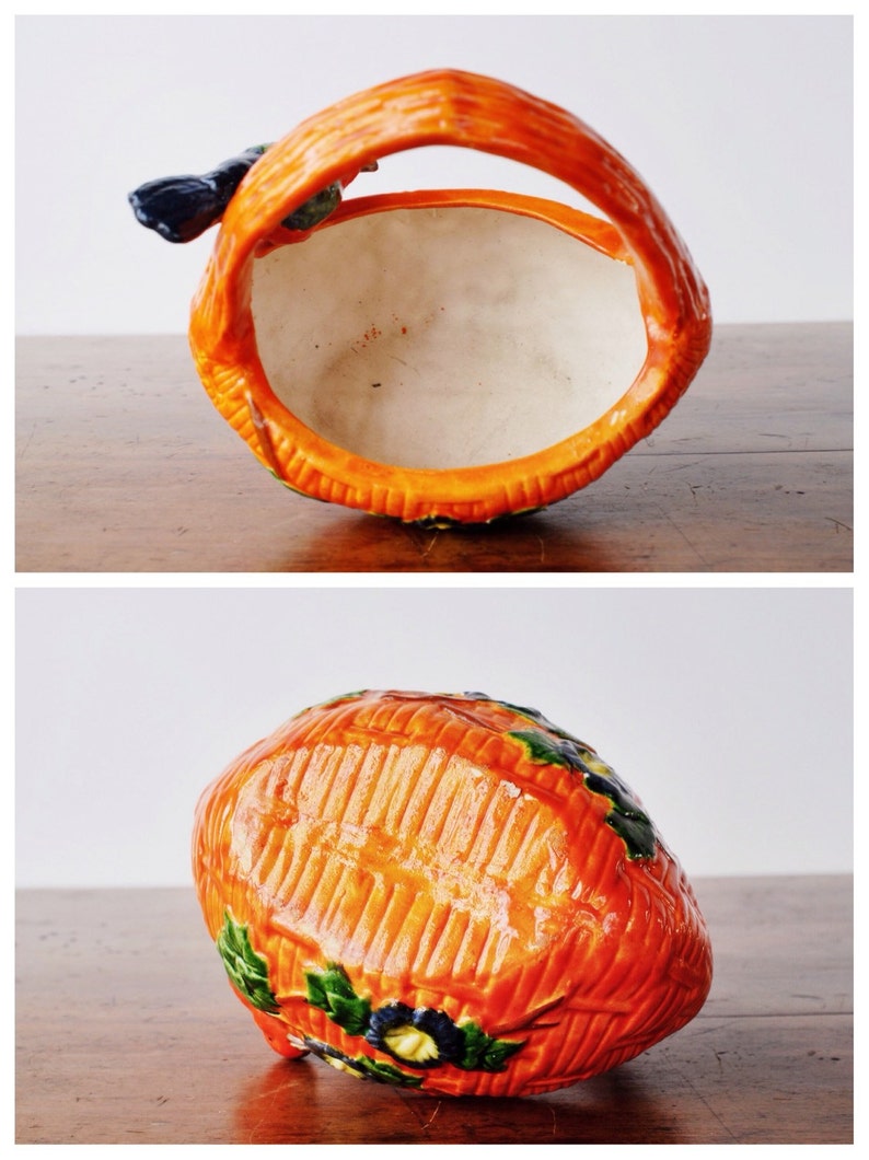May include: A ceramic basket in orange, with a handle and a textured surface. The interior is white. It has green and blue floral details. The handle mirrors the basket's design. Measurements are in centimetres.