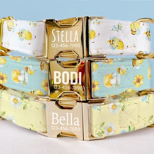 May include: Three personalised dog collars stacked. The top collar is white with yellow bees and the name "Stella". The middle collar is teal with bees and sunflowers, with the name "Bodi". The bottom collar is yellow with flowers and the name "Bella".