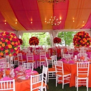 May include: A colourful event space with orange and pink decor. Tables are set with orange and pink tablecloths, white chairs, and floral centrepieces. The tent ceiling has striped orange and pink fabric.