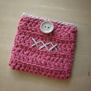 May include: A pink crocheted pouch with a white button and white stitching in the shape of an 'X'.