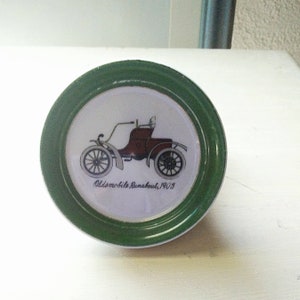 May include: A green and white ceramic coaster with a vintage car illustration and the text "Oldsmobile Runabout, 1903".