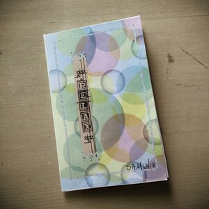 May include: A light blue card with a white stitched border and a colorful background of overlapping circles. The word "RELAX" is spelled out in black letters on a brown paper strip. The card is signed "SAM 1213".