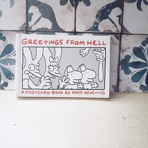 May include: A white postcard book titled "GREETINGS FROM HELL" with cartoon illustrations. The book is by Matt Groening. The cover features black and white line drawings of cartoon characters.