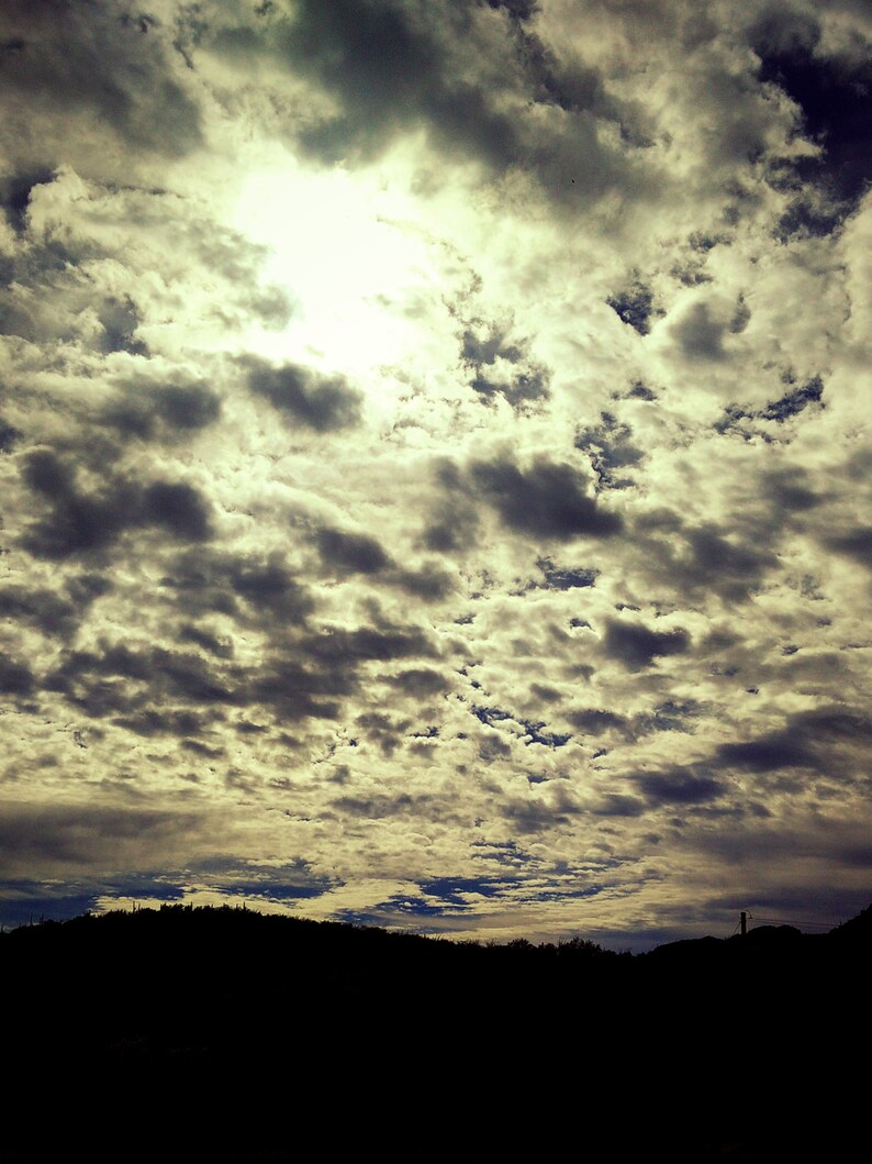 May include: A cloudy sky with a bright sun shining through the clouds. The sky is a light blue with white clouds. The sun is a bright yellow.