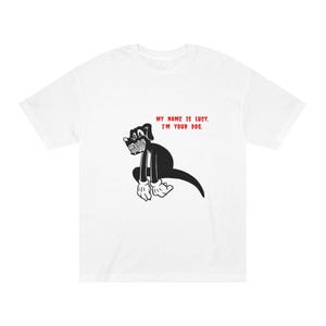 May include: White t-shirt featuring a black cartoon dog with a menacing grin. The dog is sitting with its arms and legs crossed. Red text above the dog reads, "MY NAME IS LUCY, I'M YOUR DOG."