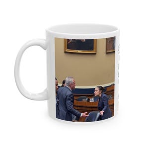 May include: White ceramic mug featuring a photograph of people in a room with paintings on the wall. The people are dressed in suits and appear to be in a discussion. The mug has a white handle.