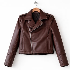 Könnte beinhalten: Braune Lederjacke mit asymmetrischem Reißverschluss, Reverskragen und gesteppten Schultern. Die Jacke hat lange Ärmel mit Reißverschlussmanschetten und eine kleine Vordertasche. Sie hängt an einem Holzkleiderbügel.
