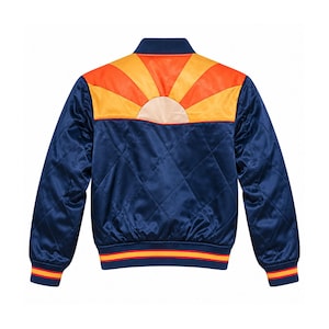 Könnte beinhalten: Eine gesteppte Bomberjacke in Marineblau mit Satin-Finish. Der obere Rückenbereich zeigt eine leuchtend orange und gelbe Sonnenstrahl-Grafik. Kragen, Ärmelbündchen und Saum sind gerippt und mit marineblauen, orangen und gelben Streifen versehen.