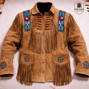 Könnte beinhalten: Hellbraune Wildlederjacke mit Fransen und dekorativen Perlenarbeiten. Die Jacke hat einen Kragen, eine Knopfleiste und Taschen mit Perlenakzenten. Schultern und Taschen haben Fransen. Die Jacke hat ein indianisches Design.