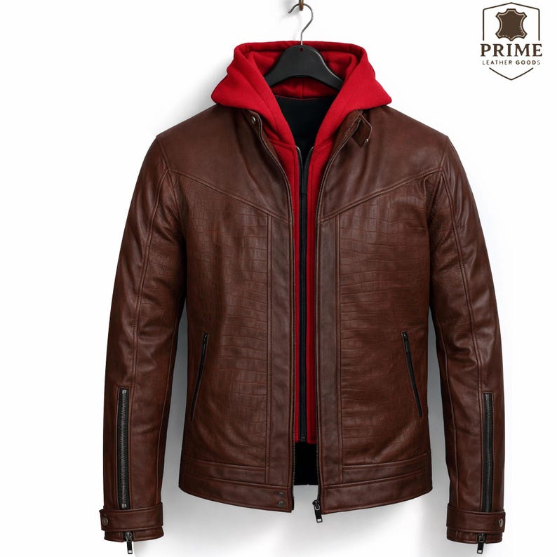 May include: A brown leather jacket with a textured finish, featuring a front zipper closure, zippered side pockets, and zippered cuffs. A bright red hooded sweatshirt is layered underneath the jacket. The logo PRIME LEATHER GOODS is visible.