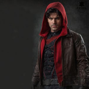 May include: A dark brown leather jacket featuring a red hooded layer underneath. The jacket is worn over a black tactical vest with segmented padding and red accents. A logo in the top right corner displays the text PRIME LEATHER JACKET.