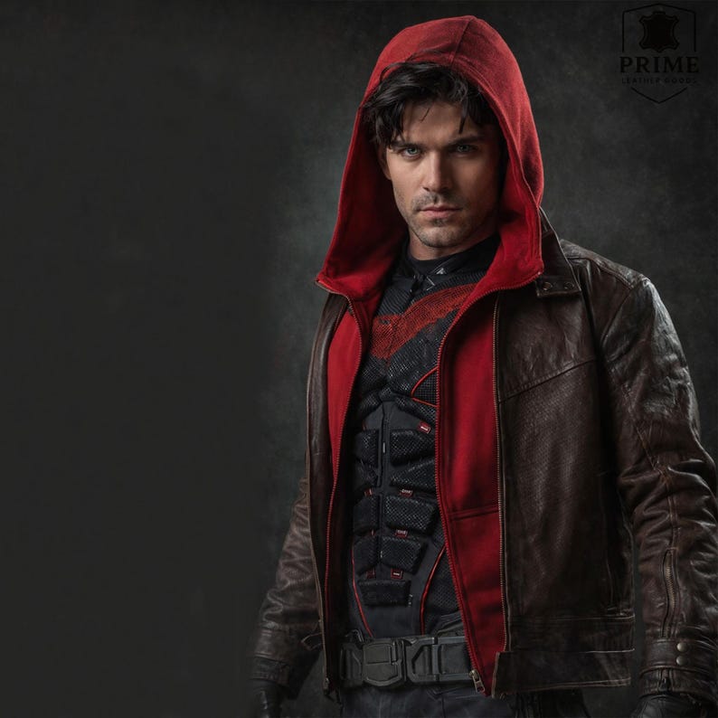 May include: A dark brown leather jacket featuring a red hooded layer underneath. The jacket is worn over a black tactical vest with segmented padding and red accents. A logo in the top right corner displays the text PRIME LEATHER JACKET.
