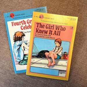 May include: Two vintage paperback books. One is titled "Fourth Grade Celebrations" and the other is "The Girl Who Knew It All." Both books feature illustrations of children and are from the "A Dell Yearling Book" series.