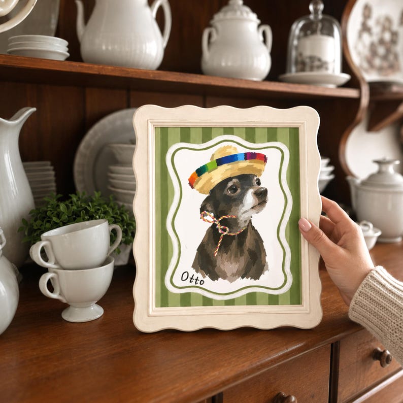 May include: A framed print featuring a portrait of a dark-furred dog wearing a colorful sombrero and a thin patterned neck tie. The dog is positioned against a green and white striped background with a scalloped border. The name Otto is written below.
