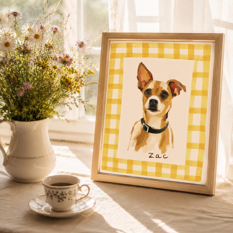 May include: A framed portrait of a brown and white dog wearing a black collar, set against a yellow and white gingham border. The name Zac is written in black script below the dog. The artwork is displayed in a light-colored wooden frame.