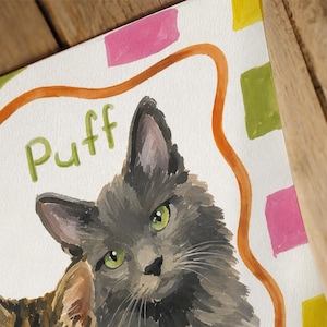 May include: A watercolor painting of a fluffy gray cat with green eyes. The word Puff is written in green letters above the cat. The background features a wavy orange line and scattered pink, yellow, and green rectangular shapes on white paper.