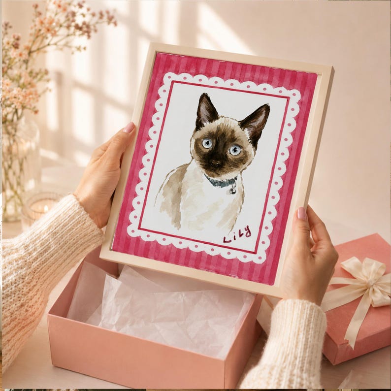 May include: A framed watercolor illustration of a Siamese cat with blue eyes and a dark face mask, wearing a collar. The artwork features a white scalloped border on a pink striped background with the handwritten name Lily in the bottom corner.