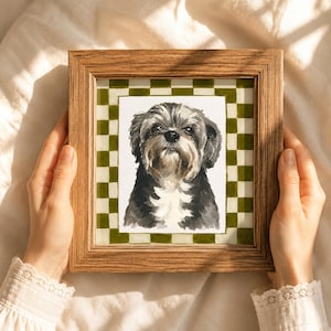 May include: A square wooden frame containing a watercolor painting of a small dog with black, gray, and white fur. The dog is centered against a white background, which is surrounded by a border featuring a green and white checkered pattern.