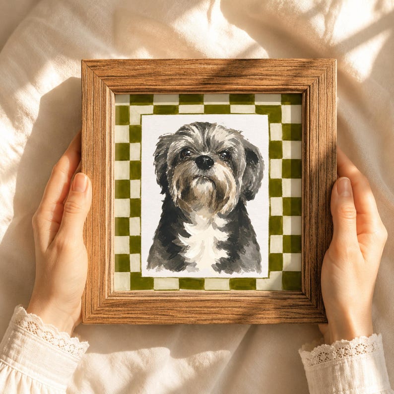 May include: A square wooden frame containing a watercolor painting of a small dog with black, gray, and white fur. The dog is centered against a white background, which is surrounded by a border featuring a green and white checkered pattern.