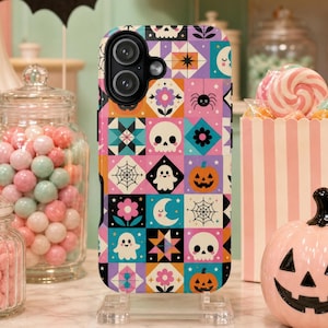 May include: A smartphone case featuring a colorful grid pattern of Halloween-themed icons including ghosts, jack-o'-lanterns, skulls, spiders, spiderwebs, flowers, stars, and crescent moons in shades of pink, orange, purple, teal, and black.