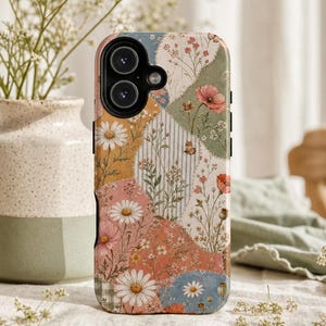 Puede incluir: Una funda para smartphone con un diseño de patchwork de varias ilustraciones florales, incluyendo margaritas y amapolas, sobre tonos apagados de verde salvia, rosa empolvado, amarillo mostaza y azul suave con sutiles patrones de rayas y cuadros.