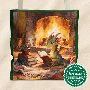 Könnte beinhalten: Tragetasche mit einer Aquarellillustration eines grünen Drachen, der vor einem Kamin ein Buch liest. Eine Teekanne steht auf einem Stapel Bücher. Die Tasche hat einen grünen Rand und cremefarbene Griffe.