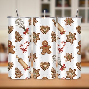 May include: Three white insulated tumblers with a festive gingerbread cookie pattern. The design includes gingerbread men, stars, hearts, Christmas trees, candy canes, rolling pins, and whisks. Each tumbler has a silver straw.