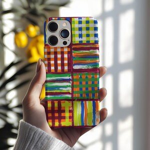 Puede incluir: Funda de teléfono colorida con un diseño de patchwork. Los cuadrados presentan patrones de rayas y cuadros en tonos naranja, verde, azul y morado. La funda tiene un acabado brillante.