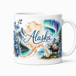 May include: A white ceramic mug featuring a watercolor illustration of the state of Alaska with the text Alaska in blue script. The design includes blue forget-me-not flowers, snow-capped mountains, a moose, pine trees, and the aurora borealis.