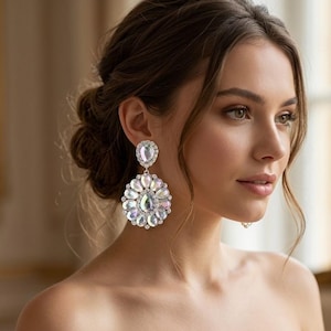 May include: A pair of statement earrings featuring a small teardrop-shaped crystal at the top, connected to a large, circular cluster of iridescent, pear-shaped crystals arranged in a floral pattern, all set in a silver-toned metal frame.