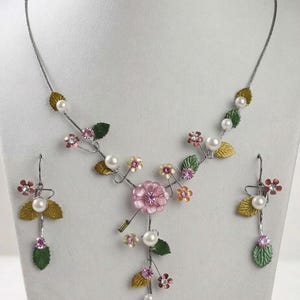 May include: A jewelry set consisting of a necklace and matching drop earrings. The pieces feature silver-tone wire branches adorned with small white faux pearls, green and gold metal leaves, and tiny pink and orange flowers with crystal centers.