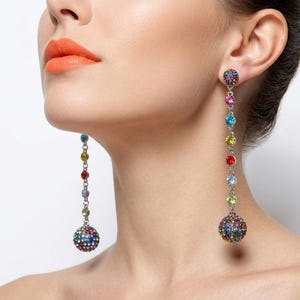 May include: Dangling earrings with a silver chain and colorful, round, jeweled accents. The earrings feature a large, jeweled ball at the bottom and a smaller jeweled ball at the top, with a series of colorful jewels in between.