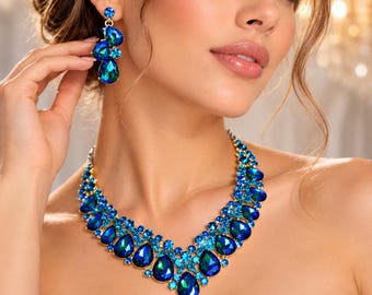 May include: A jewelry set consisting of a necklace and drop earrings featuring faceted blue and teal crystals set in gold-tone metal. The necklace has a V-shaped arrangement of teardrop and round stones, while the earrings feature a cluster design.