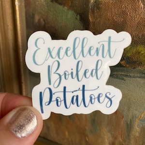 May include: A white sticker with the words "Excellent Boiled Potatoes" in a blue script font. The sticker is held in front of a painting with brown and gold tones.