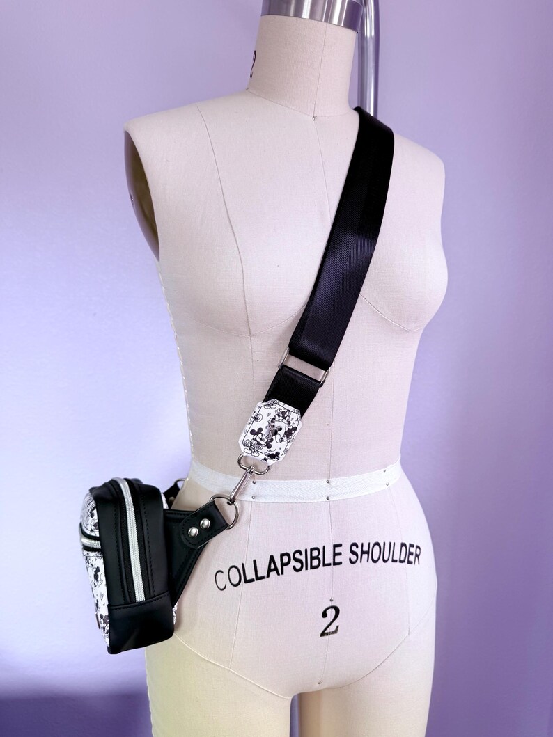 Peut inclure: Sac banane noir et blanc avec une bandouli&egrave;re assortie. La bandouli&egrave;re a une boucle d&eacute;corative avec un motif noir et blanc. Le sac banane est attach&eacute; &agrave; la bandouli&egrave;re avec un anneau en m&eacute;tal argent&eacute;.