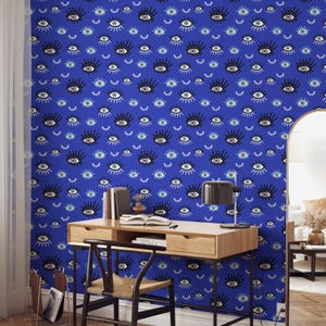 May include: A blue wall covered in a repeating pattern of stylized eyes in black, white, and light blue. The eyes vary in size and orientation. A wooden desk, chair, and lamp are in front of the wall.